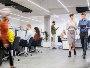 Busy office with employees walking around and others working at their desks.