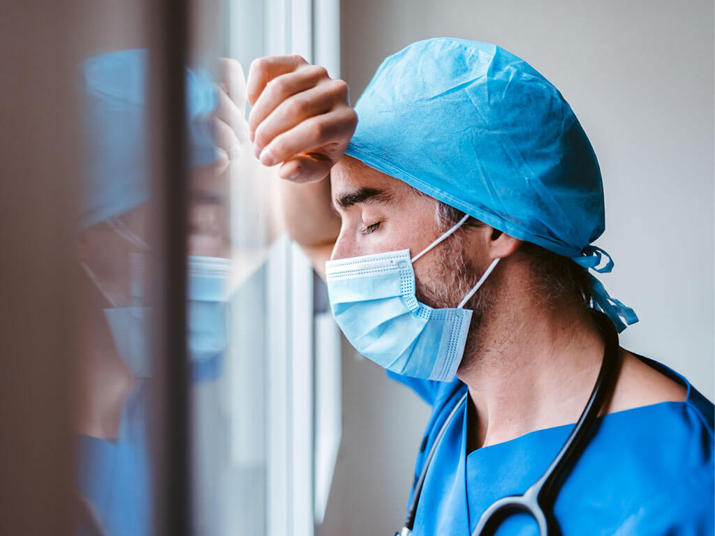 Doctor resting head on forearm on window.