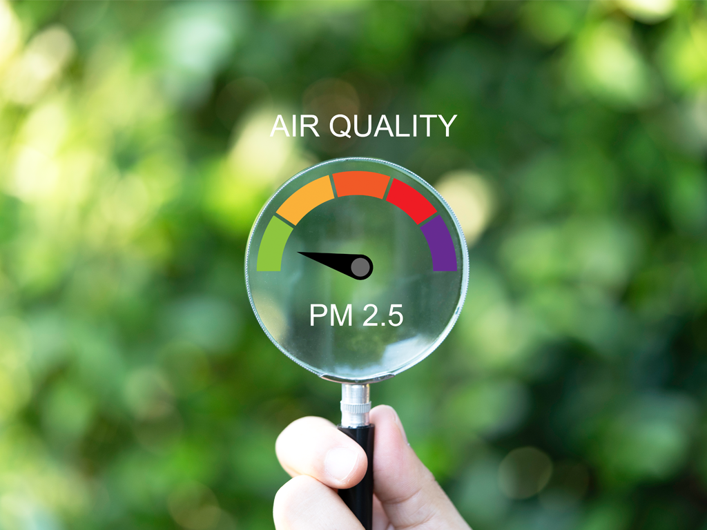A hand holding a magnifying glass with a PM 2.5 scale imprinted on it outside. The EPA updated Particulate Matter standards so how does this affect you?