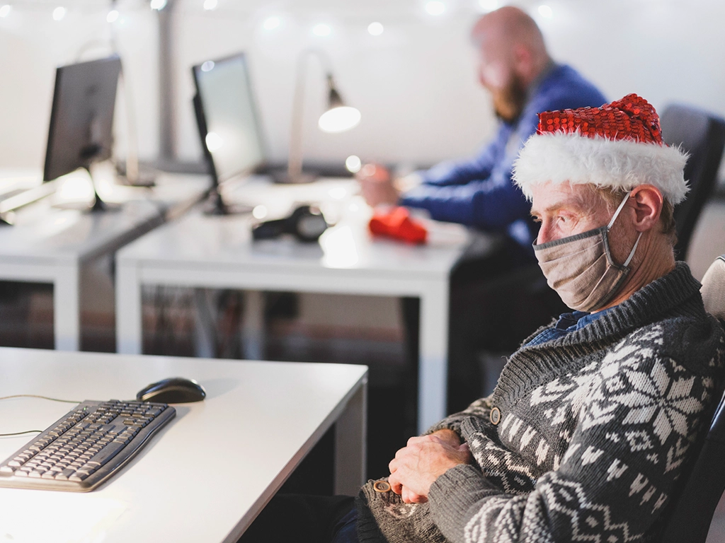 Man sitting at his desk in his office with a mask and a Santa hat during flu season.