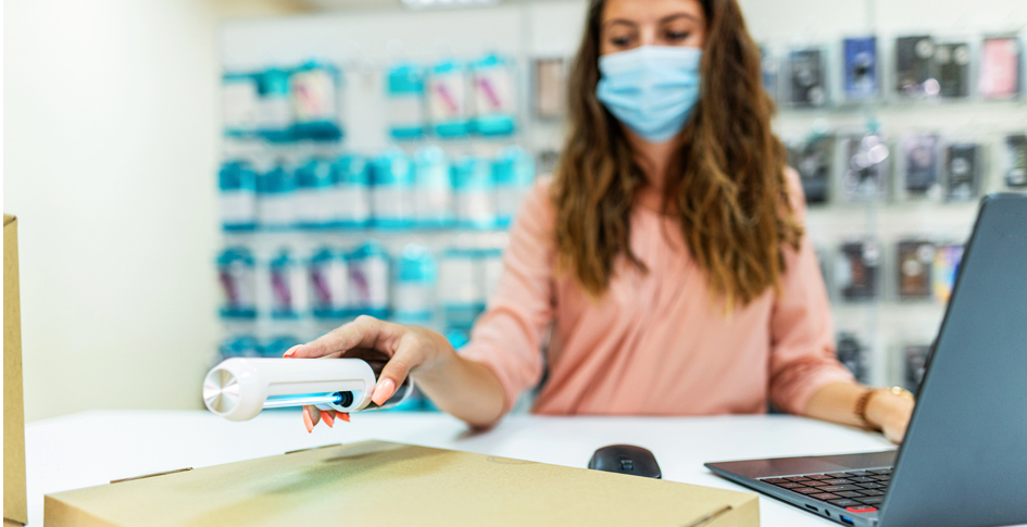 Woman at a desk using a handheld UV wand to sanitize a box.
