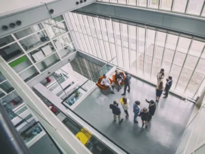 A group of people standing in a room with windows, ASRAE 241 proposes minimum requirements to reduce risk of disease transmission to help keep all occupants of your business safe.