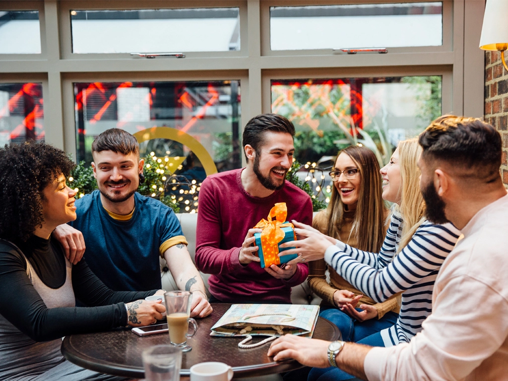 A group of people sitting around a table with a gift, new CDC guidelines are allowing people to return to normal routine faster than before after contracting COVID.