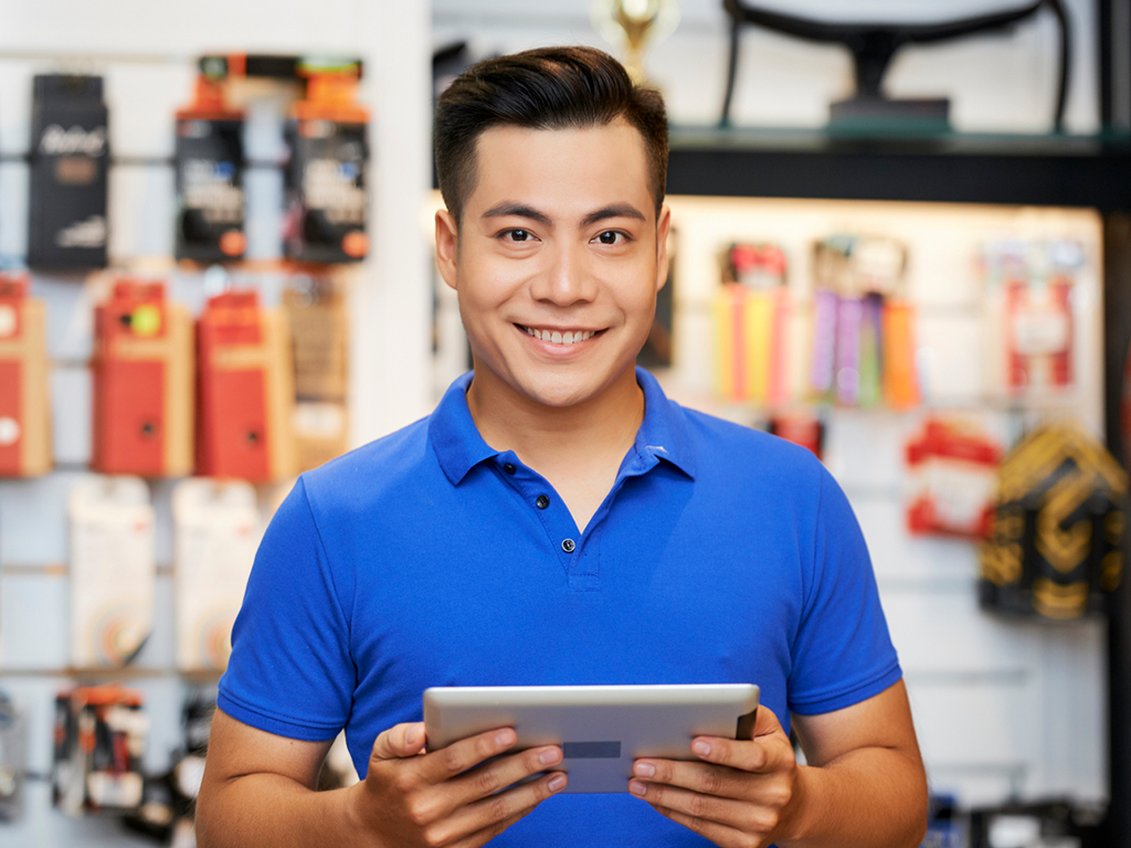 Salesman in blue polo holding a tablet in front of a storefront
