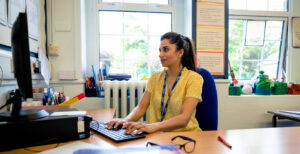 School administrator in a school working at her desk; IAQ is just as important to students as it is to staff to maintain a productive & positive learning environment.