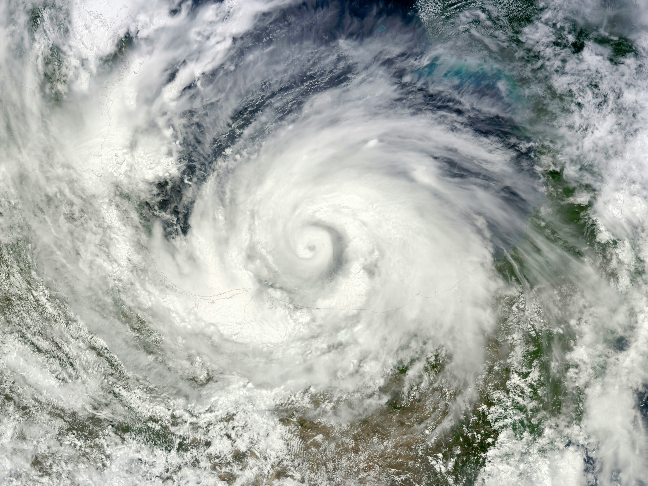 Satellite view of a powerful tropical cyclone with a broad spiral of clouds over land and sea, taken from space.